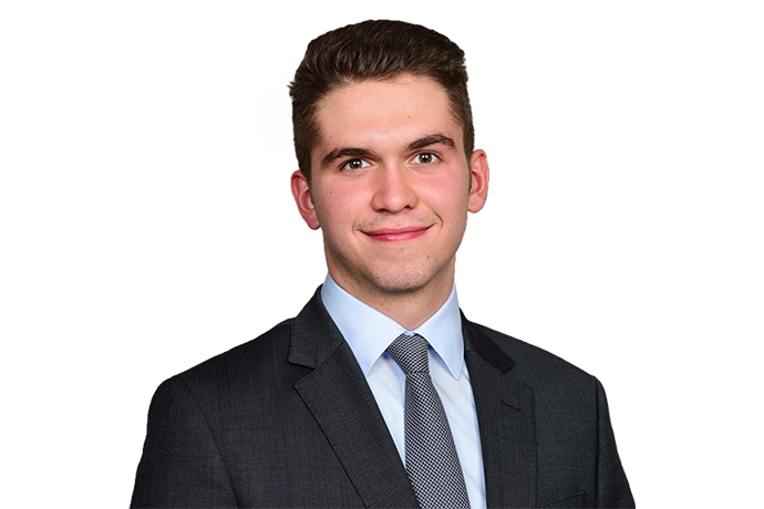 Die abgebildete Person trägt einen dunklen Anzug mit einem weißen Hemd und einem gestreiften Krawatte vor einem schwarzen Hintergrund.