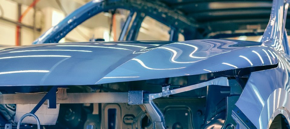 Das Bild zeigt ein unvollständiges Auto während der Montage oder in einem Produktionsprozess. Es ist deutlich zu erkennen, dass das Fahrzeug sich noch im Herstellungsstadium befindet, da einige Teile fehlen und es in einer Werkstatt oder industriellen Umgebung platziert ist. Der Fokus scheint auf der Fahrzeugstruktur und spezifischen Komponenten der Karosserie zu liegen, die darauf hinweist, dass technische Arbeiten durchgeführt werden. Die glänzende Oberfläche des Materials lässt darauf schließen, dass es sich möglicherweise um ein kürzlich lackiertes Fahrzeug handelt.