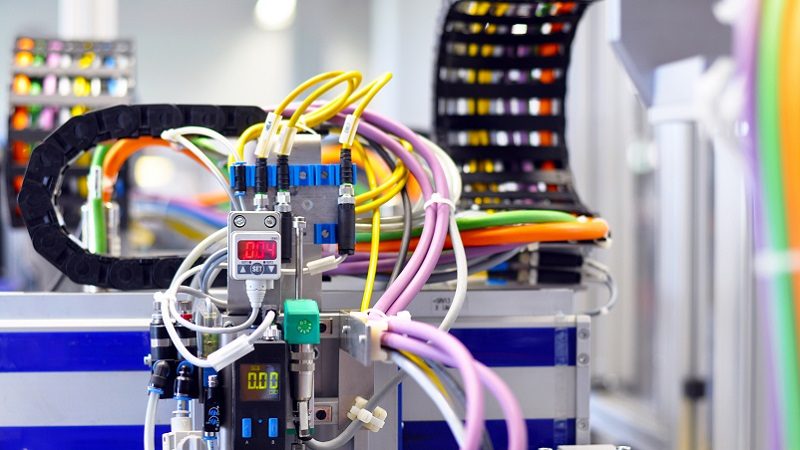 Das Bild zeigt ein komplexes elektrisches Schaltsystem oder eine Steuerungseinheit, wie man es in industriellen Anwendungen finden könnte. Zu erkennen sind mehrere Kabel mit unterschiedlichen Farben, die in eine Vielzahl von Steck- und Schaltgeräten eingesteckt sind.
**Details zu beachten:**
- **Kabel und Leitungen:** Die unterschiedlichen Farben der Kabel deuten auf verschiedene Signale oder Stromkreise hin, die organisiert und fehlerfrei verbunden werden müssen.
- **Digitale Anzeigen:** Es sind digitale Anzeigen zu sehen, die möglicherweise Informationen wie Stromstärke oder andere relevante elektrische Parameter anzeigen.
- **Verbindungsstücke und Klemmen:** Diese sind essentiell für das sichere und effiziente Funktionieren solcher Systeme.
- **Organisierte Kabelführung:** Die Kabel sind durch Kabelträgern geführt, um Ordnung und Stabilität sicherzustellen.
Das Bild vermittelt die Komplexität und Präzision, die für die Verkabelung und den Betrieb von industriellen elektrischen Systemen notwendig sind.